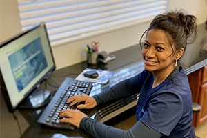 dental worker typing at desk while smiling at camera
