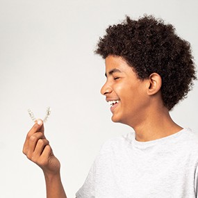Teenage boy smiling while holding clear aligner