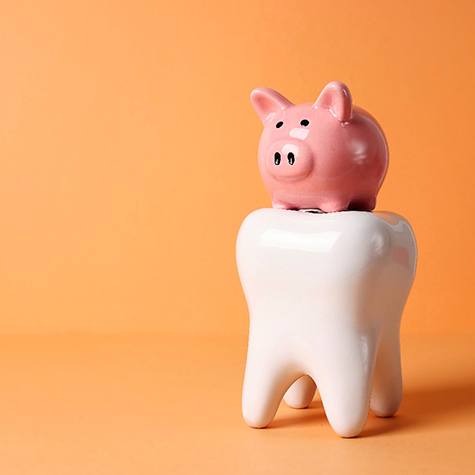 a model tooth on top of a piggy bank