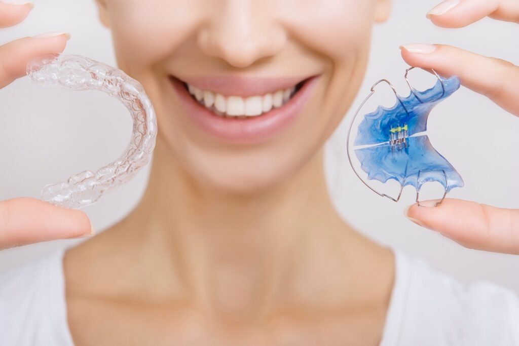 Closeup of smiling woman holding a traditional retainer and modern retainer