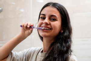 a patient with braces smiling and brushing their teeth