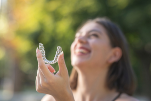 a patient smiling and holding their Invisalign aligner