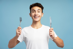 a patient with braces smiling and holding a fork and knife
