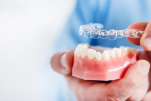 a person holding an Invisalign aligner and model teeth