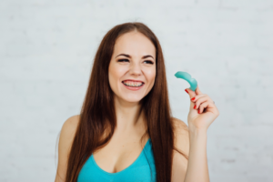 a teen with braces smiling and holding their mouthguard